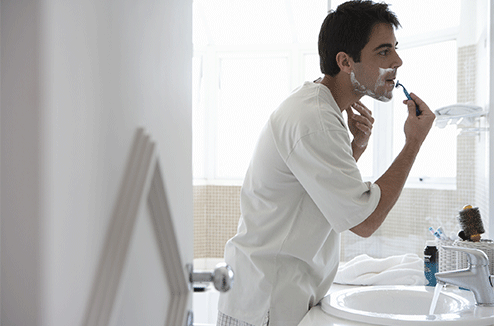 Un homme se rase devant son miroir de salle de bain
