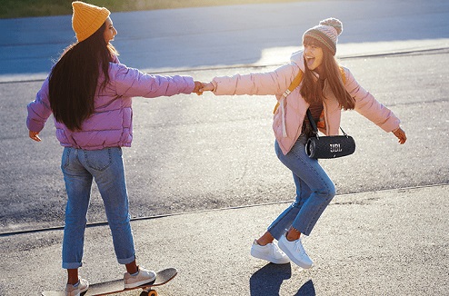 2 jeunes filles font du skate en écoutent une enceinte sans fil JBL