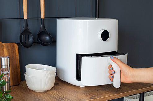 Un airfryer est très utile dans une cuisine ! Mais lequel choisir ? Une main de femme ouvrant un airfryer à 1 tiroir blanc