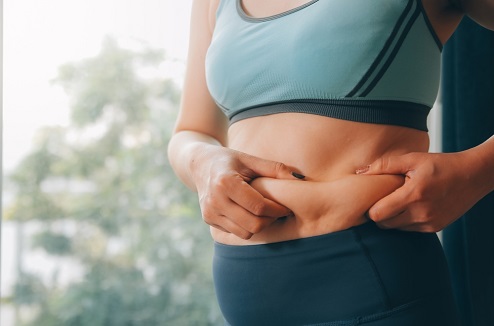 Un femme tient des plis de son ventre entre ses mains